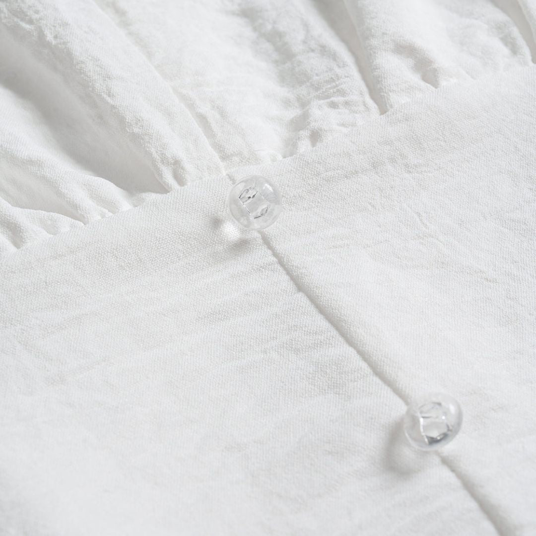 Vit blus med spetskant, korta puffärmar och transparenta knappar